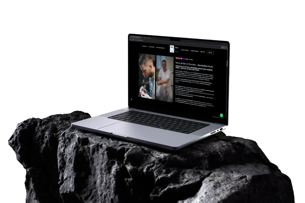 Laptop mit geöffneter Black & White Tattoo Studio Website auf einem dunklen Stein vor schwarzem Hintergrund. Zu sehen ist eine Inhaltsseite mit Tattoo-Künstlern, Fotos und ausführlichem Text in einem kontrastreichen, dunklen Webdesign.