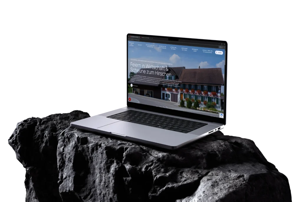 Website-Mockup der Wirtschaft & Scheune zum Hirschen: Laptop-Darstellung der Startseite mit historischer Fachwerkfassade, Blumenbalkonen und klarer Navigation, präsentiert auf einem Steinpodest vor schwarzem Hintergrund.